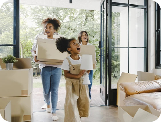 Foto de uma família com os filhos e a mãe entrando em sua casa carregando caixas em suas mãos.